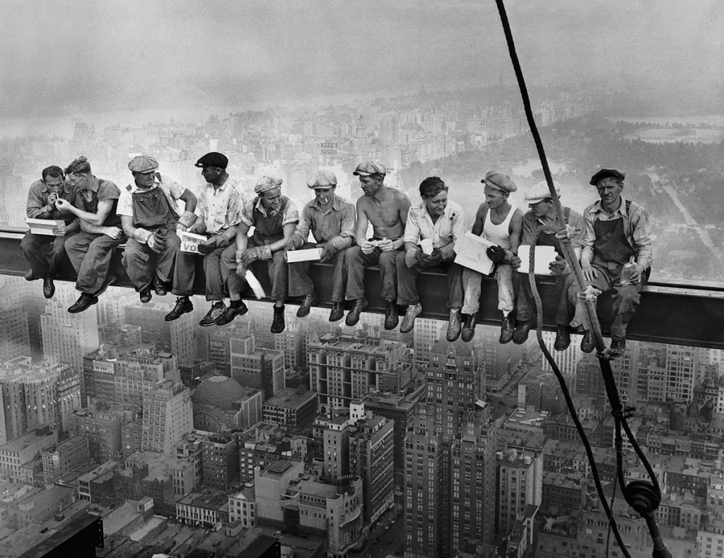 a group of construction men having lunch atop a skycraper crane